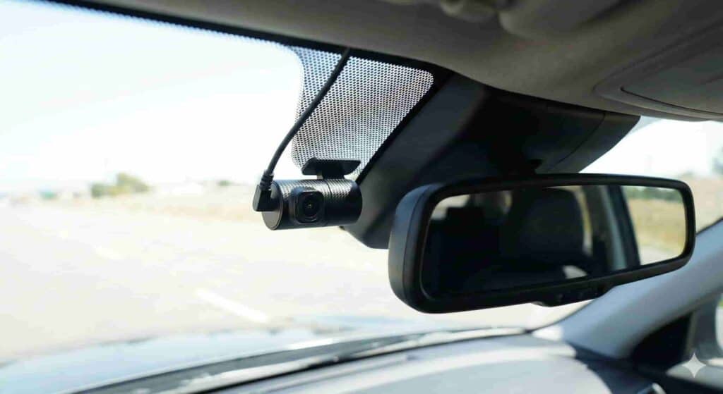 Vista interior de una dashcam pequeña instalada correctamente detrás del espejo retrovisor central, en la zona superior del parabrisas, cumpliendo con la normativa legal al no obstaculizar la visión del conductor.