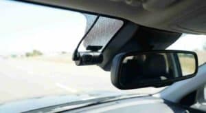 Vista interior de una dashcam pequeña instalada correctamente detrás del espejo retrovisor central, en la zona superior del parabrisas, cumpliendo con la normativa legal al no obstaculizar la visión del conductor.